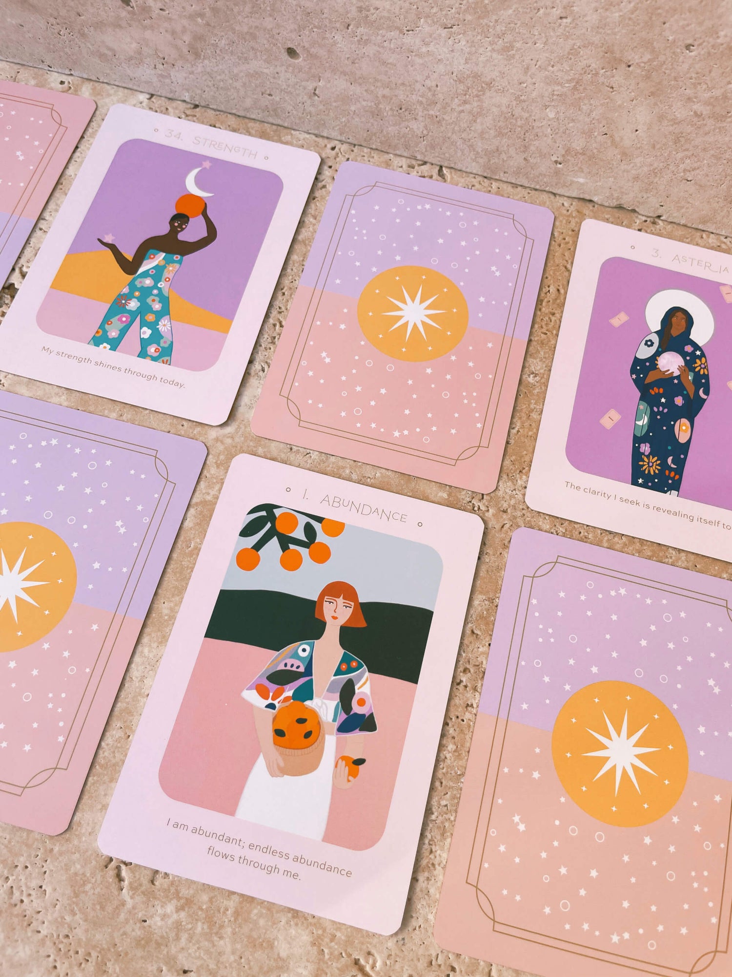 Eunoia Daily Rituals Oracle Deck cards on a pink stone table. The abundance card is face up. It reads "I am abundant; endless abundance flows through me."