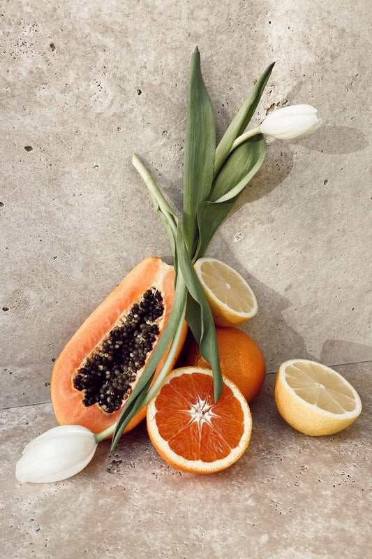 A fresh arrangement of white tulips and fruit on a stone backdrop.