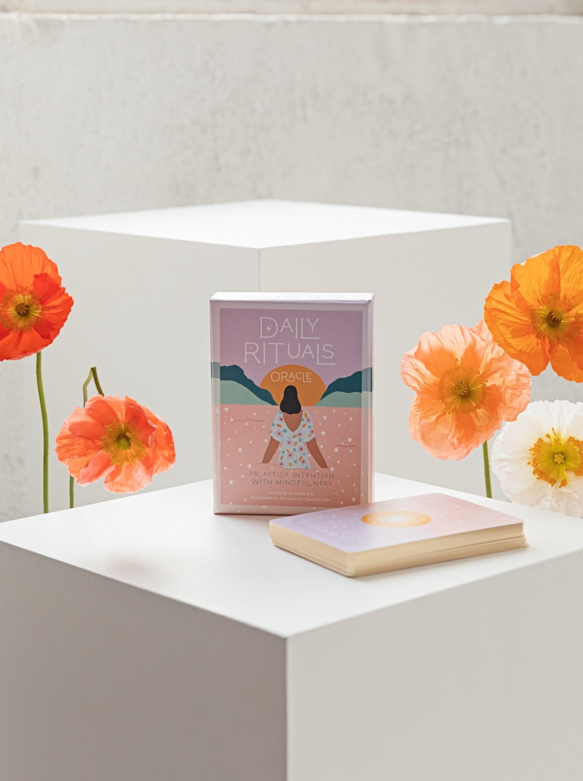 Eunoia Daily Rituals deck sitting on a white plinth with fresh poppies on either side.