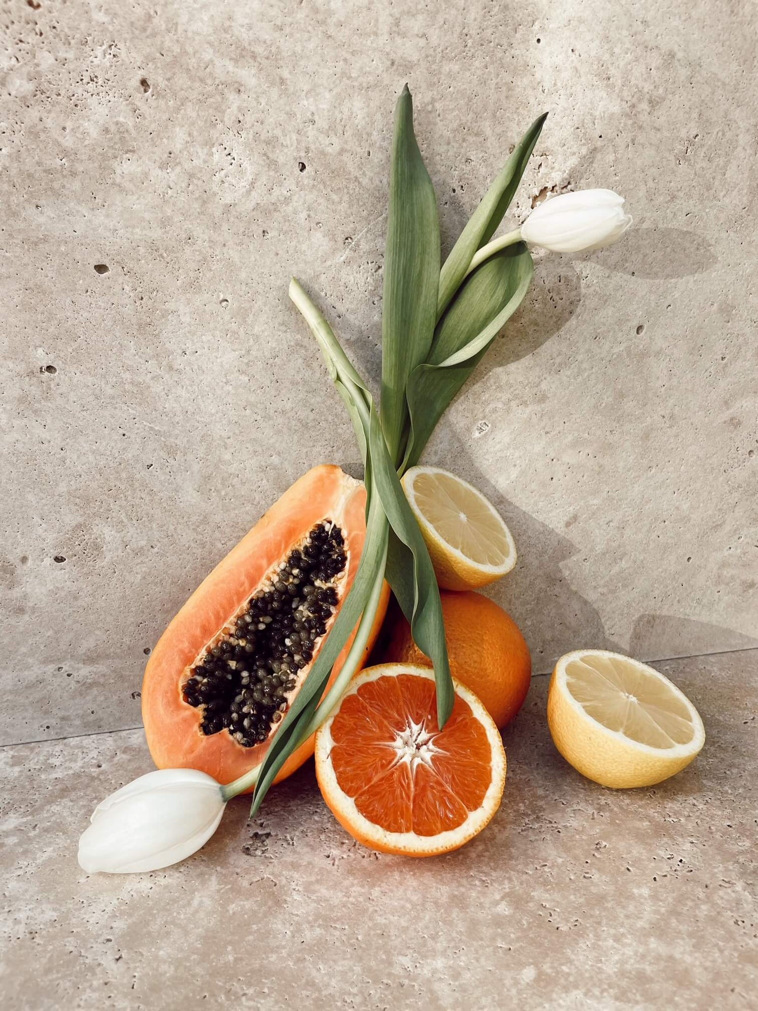 Cut fruit with two white tulips on a stone backdrop.