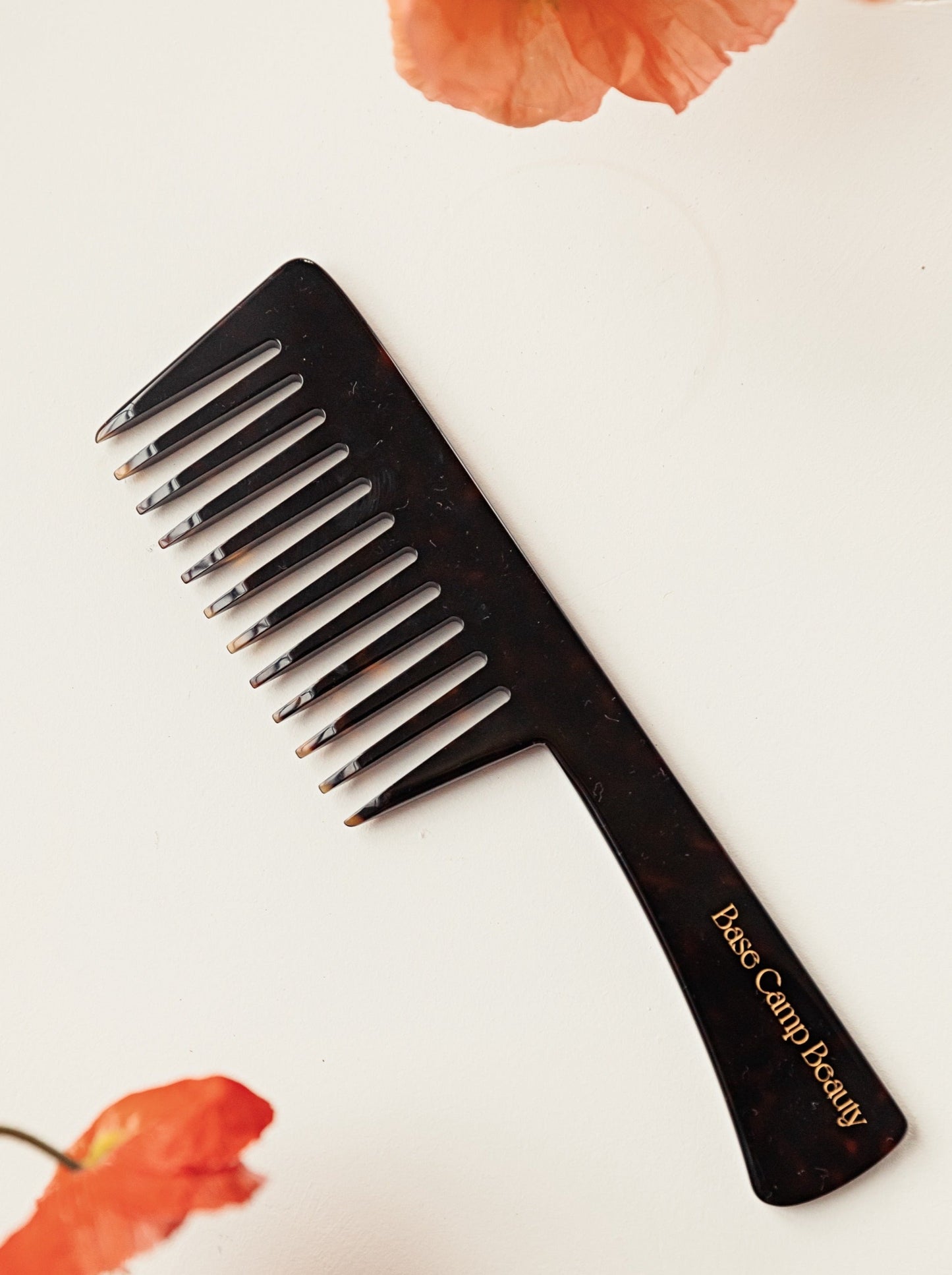 Base Camp Beauty tortoise comb sitting flat on a white background with a poppy either side 