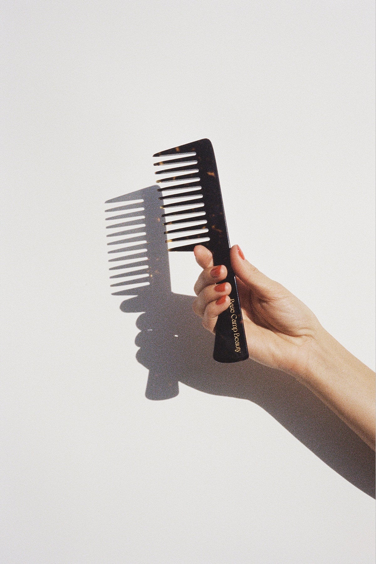 A woman's hand holding a Base Camp Beauty Grand Comb in tortoise.