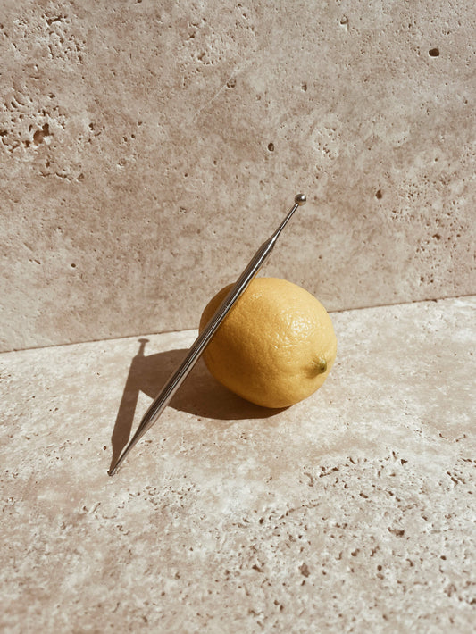 Base Camp Beauty Reflexology Pen leaning on a whole lemon. The background is a stone benchtop.