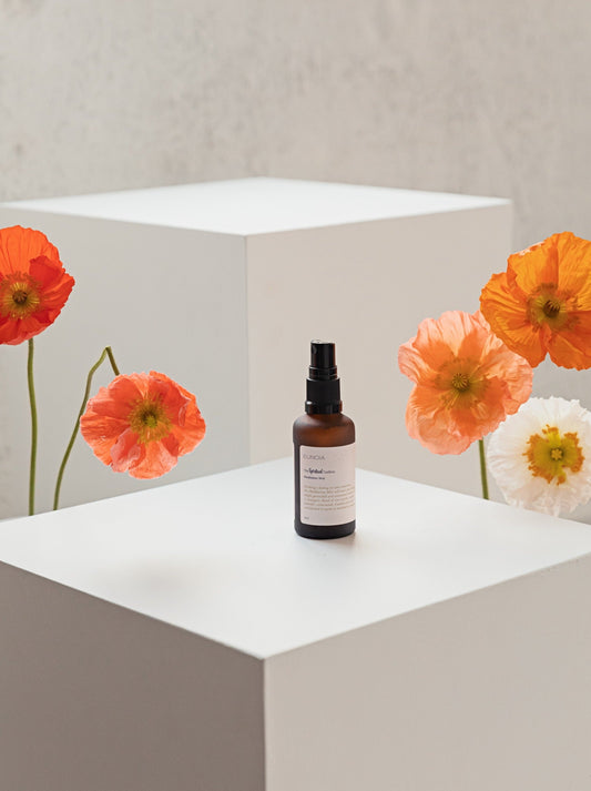 bottle of meditation. mist sitting on a white plinth with fresh orange poppies either side