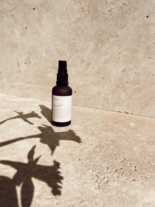 A bottle of Eunoia Abundance mist on a stone benchtop with a heavy shadow cast from flowers in the foreground.