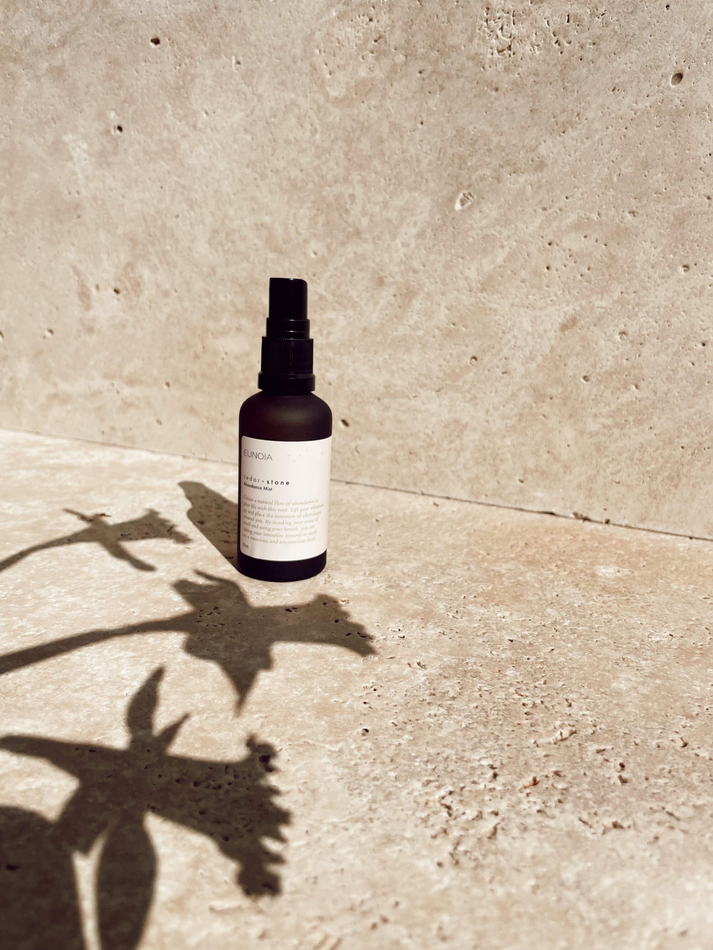 A bottle of Eunoia Abundance mist on a stone benchtop with a heavy shadow cast from flowers in the foreground.