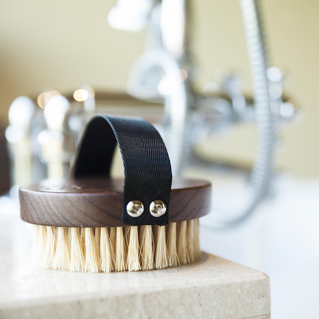 A Stass & Co dry body brush on a stone bathroom counter.